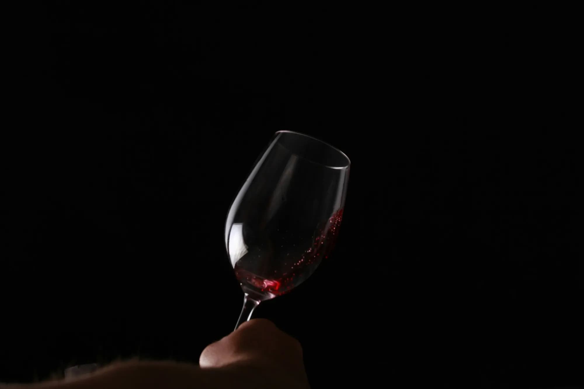 A hand swirling a glass of red wine against a dark background